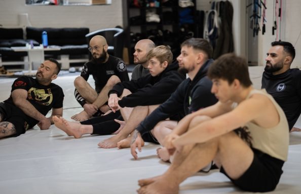 Gruppe von acht Personen sitzt im Trainingsraum für Kampfsportübungen.